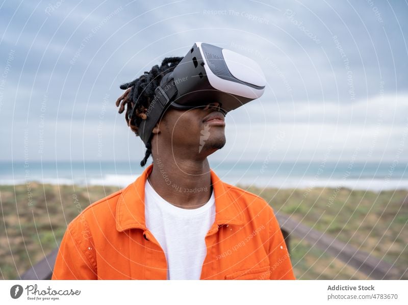 Schwarzer Mann erforscht virtuelle Realität an der Meeresküste VR Virtuelle Realität Cyberspace Promenade futuristisch Schutzbrille Ufer Stauanlage Stil Brille