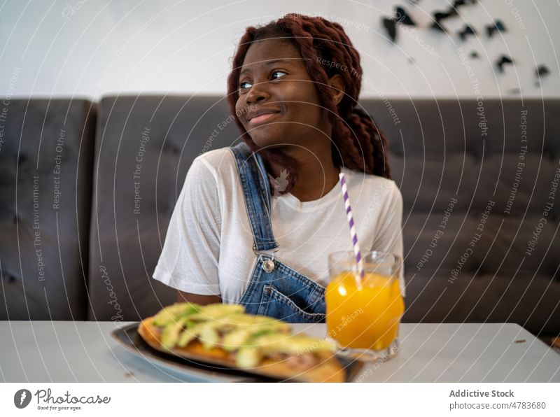 Schwarze Frau isst und trinkt Saft in einem Cafe trinken Getränk Stroh orange Lächeln Glück Café froh Erfrischung Durst Speise Mahlzeit Lebensmittel jung