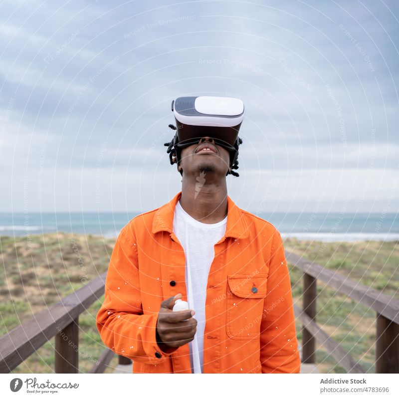 Schwarzer Mann erforscht virtuelle Realität an der Meeresküste VR Virtuelle Realität Cyberspace Promenade futuristisch Schutzbrille Ufer Stauanlage Stil Brille