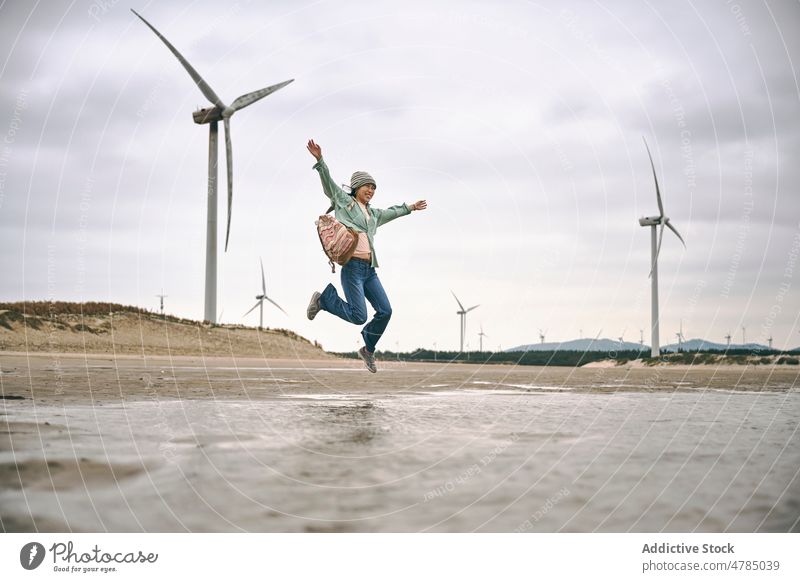 Frau springt in der Nähe von Windmühlen am Meer Energie springen asiatisches Mädchen Chinesisches Mädchen wolkig Seeküste Strand Himmel Freiheit Turbine Wetter