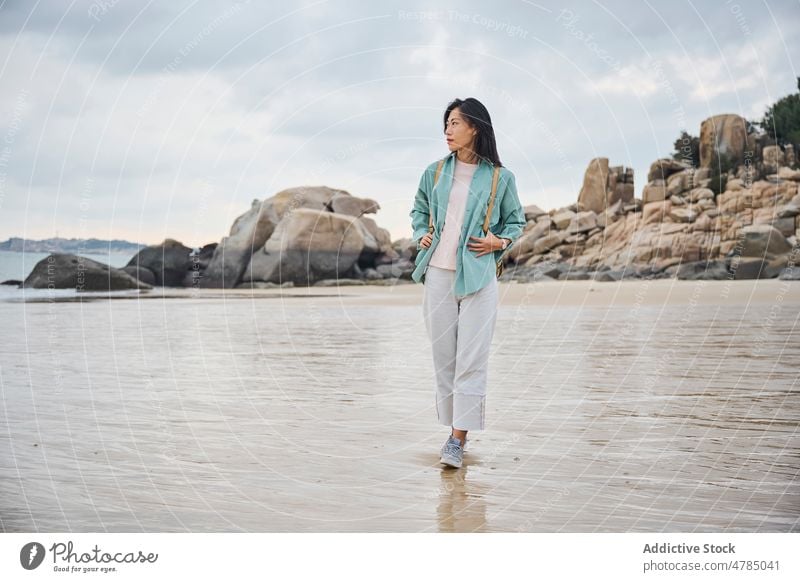 Schönes asiatisches Mädchen, das während ihrer Reise im Herbst am Strand spazieren geht Natur Steine laufen wolkig Sand Spaziergang nass nasser Sand