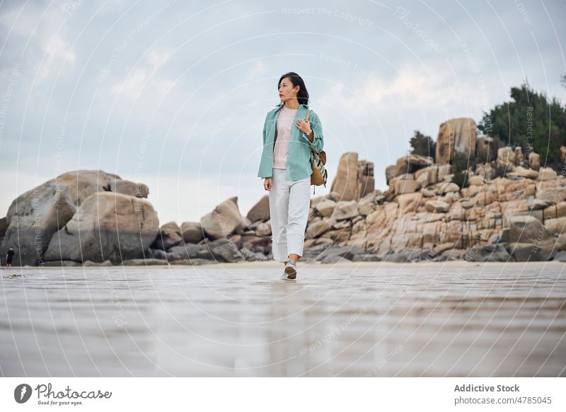Schönes asiatisches Mädchen, das während ihrer Reise im Herbst am Strand spazieren geht Natur Steine laufen wolkig Sand Spaziergang nass nasser Sand