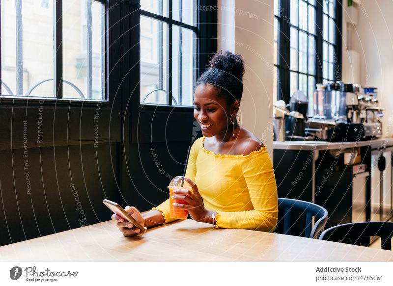 Glückliche Frau, die in einem Café telefoniert und Saft trinkt Smartphone sich[Akk] entspannen benutzend jung trinken Tasse Telefon Mobile Afroamerikaner