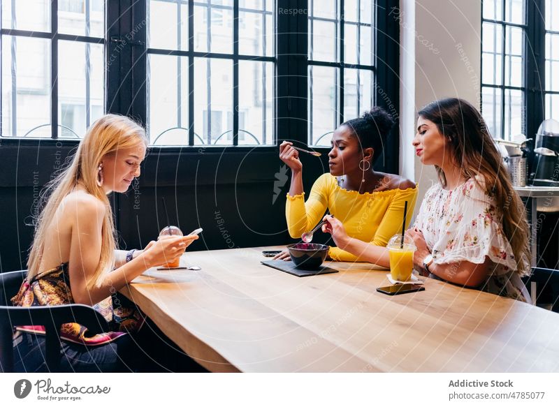 Frauen, die in einem Café gesund frühstücken und ihr Handy benutzen Browsen Smoothie Schüssel Imbissbude Supernahrung Gesundheit Freund genießen Smartphone