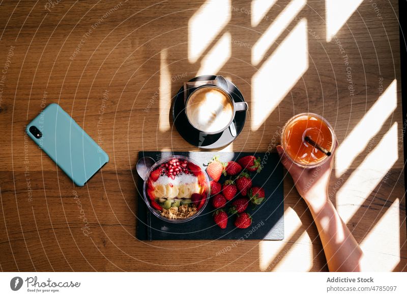 Frau frühstückt gesund und telefoniert Frühstück gesunde Ernährung Smartphone Tisch Erdbeeren Smoothie Schüssel Frucht Kaffee Lebensmittel hölzern Saft