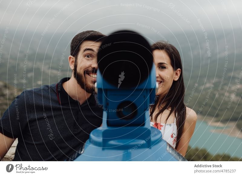 Fröhliches Paar, das sich auf der Aussichtsplattform der Stadt mit einem Fernglas vergnügt Berge u. Gebirge heiter spielerisch Spaß haben Spielen freudig