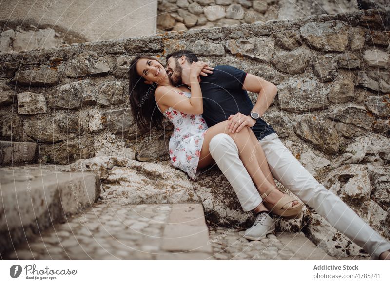 Glückliches Paar, das Spaß hat, während es auf einer Steinstraße sitzt Kuss Stadt Straße Liebe romantisch Zuneigung spielerisch lässig Umarmen kuscheln
