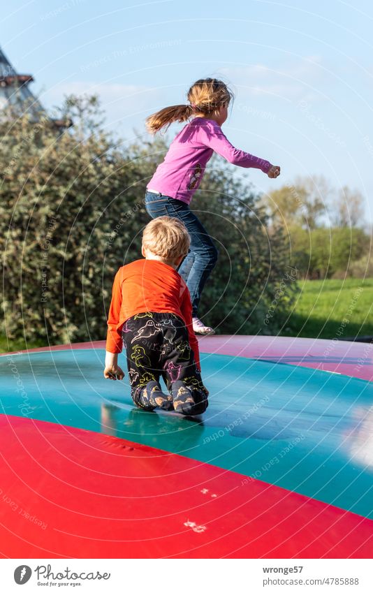 2 Kinder springen auf einem Hüpfkissen im Park hüpfen toben Bewegung Mädchen Junge Spielen Freude Außenaufnahme Kindheit Lebensfreude Farbfoto sportlich