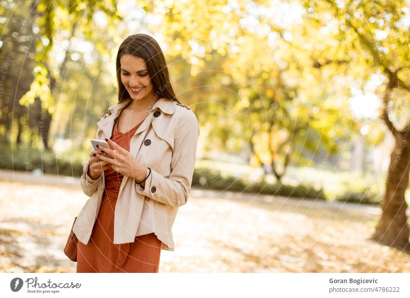Fröhliche junge Frau mit Handy im Herbstpark Park Telefon Person fallen schön Erwachsener Mitteilung Porträt Schönheit Saison Lächeln Mobile im Freien