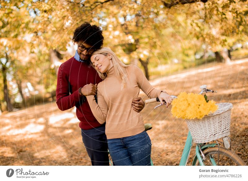 Gemischtrassiges Paar mit Fahrrad im Herbstpark Park Laubwerk fallen Blumen gelb Mann Frau jung multiethnisch Glück Freizeit Kaukasier Lächeln Zusammensein