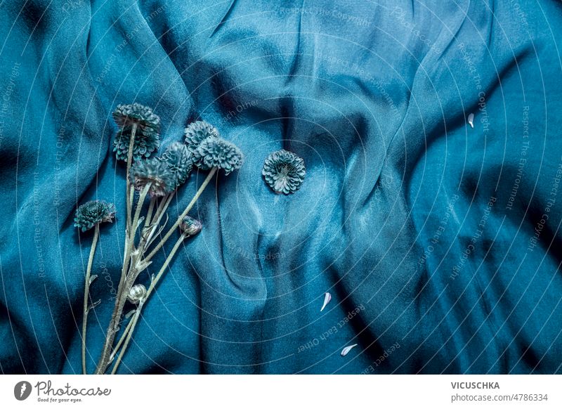 Blauer drapierter Satin-Stoff-Hintergrund mit Blumenstrauß. blau Gewebe Haufen Textil Überstrahlung blaue Blütenblätter Draufsicht Textfreiraum Blütezeit Design
