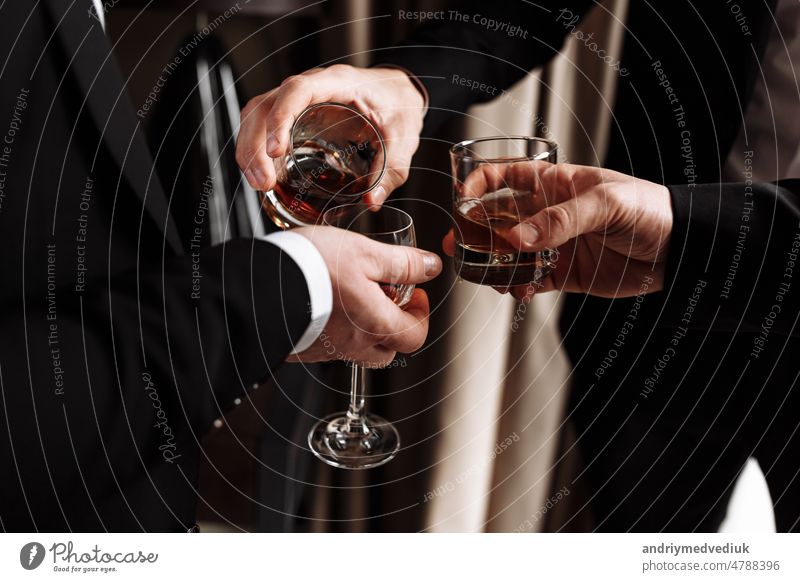 Geschäftstreffen. Männer halten Gläser mit Whiskey. Männerparty. Hand mit einem Getränk von Alkohol Mann Röstung Hände Brille jung Party Beteiligung Glück gold
