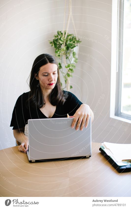 Frau, die an ihrem Küchentisch an ihrem Laptop arbeitet Erwachsener Business Pflege Kaukasier farbenfroh Mitteilung Computer dunkles Haar Schreibtisch