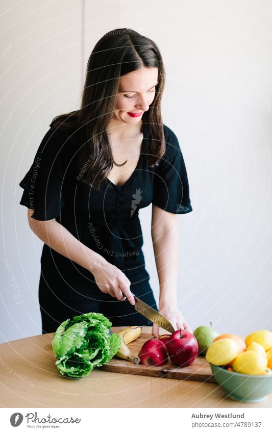 dunkelhaarige Frau schneidet Gemüse und Obst auf einem Schneidebrett Apfel Banane Kalorien Pflege Kaukasier Kanal Küchenchef Essen zubereiten geschnitten