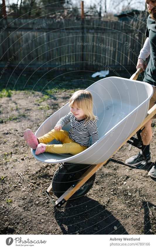 spielerischer Vater und Tochter in einer Schubkarre bei der Gartenarbeit Ackerbau Hinterhof blond Karre Kaukasier Kind Kindheit niedlich Gerät Gesicht Familie