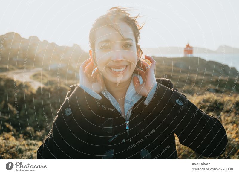 Helles und lebendiges Porträt einer jungen arabischen Frau, die an einem windigen Tag während der goldenen Stunde des Sonnenuntergangs lächelt. Sea Shore Reise und Urlaub Bild, mit einem Leuchtturm hinter. Van Leben mit Kopie Raum