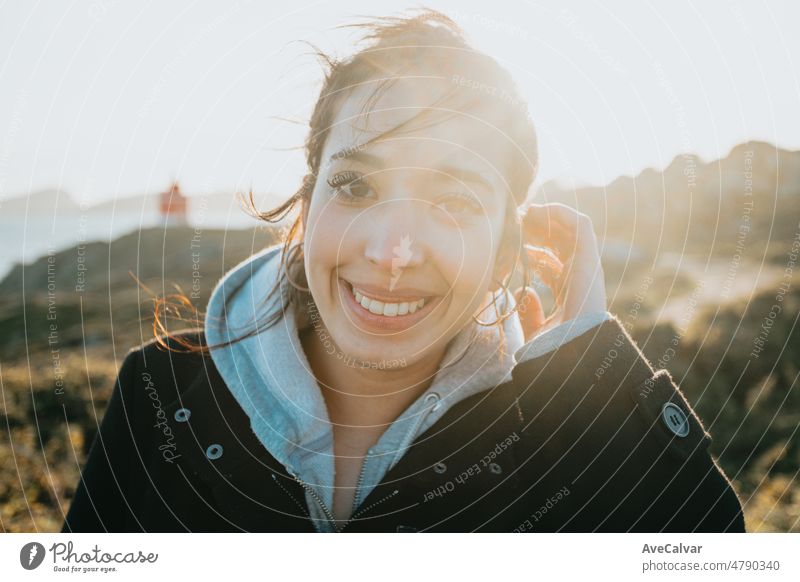 Close up Licht und lebendige Porträt einer jungen arabischen Frau lächelnd während eines windigen Tages während des Sonnenuntergangs golden hour.Sea Shore Reisen und Urlaub Bild, mit einem Leuchtturm hinter. Van Leben mit Kopie Raum