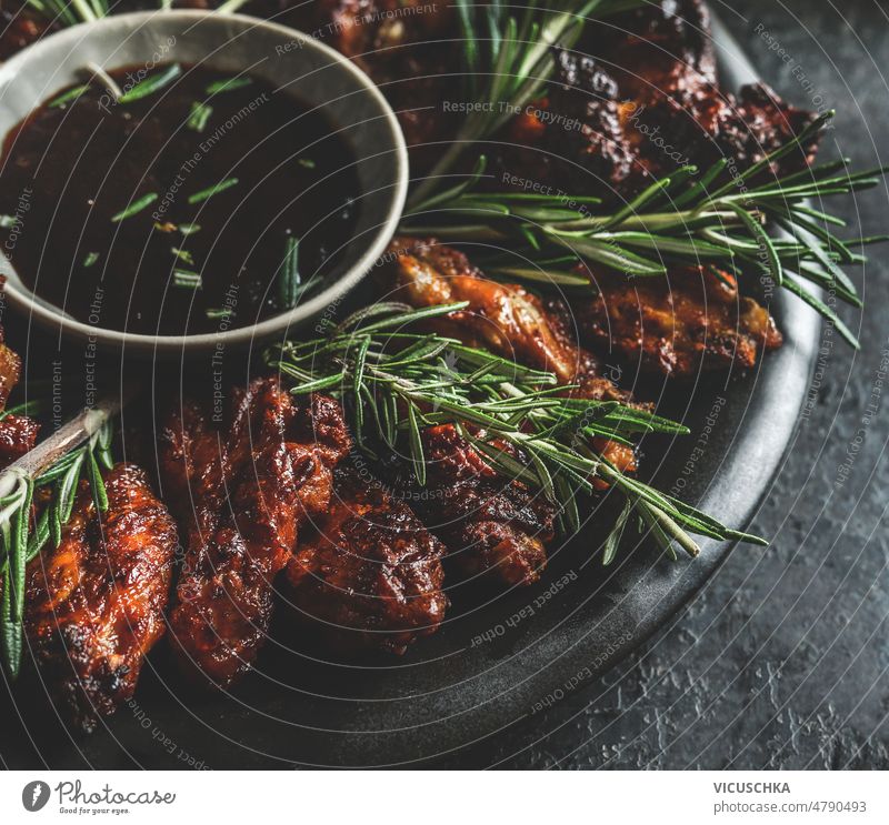 Nahaufnahme von gegrillten Hähnchenflügeln mit Rosmarin und aromatischer Barbecue-Sauce auf dunklem Hintergrund. abschließen geschmackvoll Barbecue-Soße dunkel