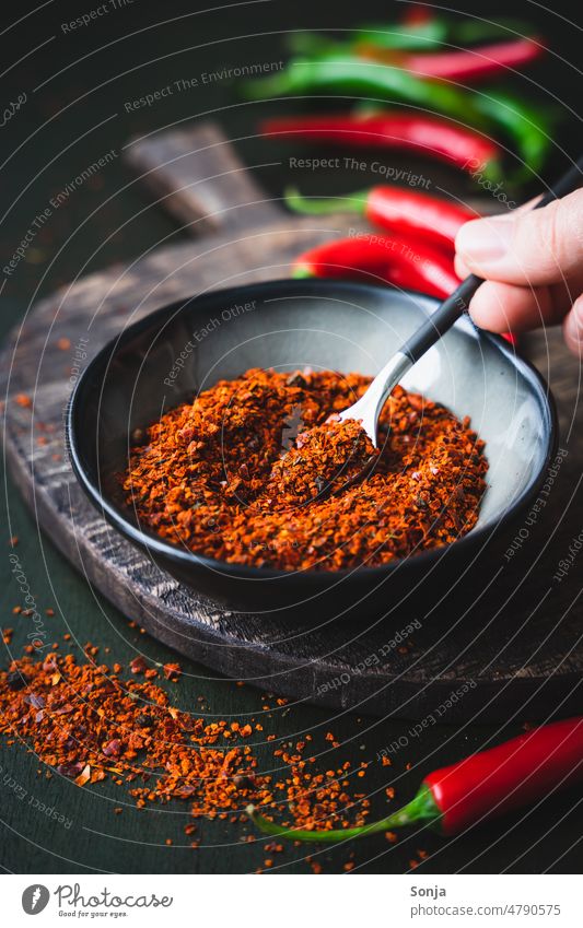 Chillipulver Gewürz in einer schwarzen Schüssel Pulver gewürz Hand Löffel rustikal Zutaten Tisch Scharfer Geschmack rot Küche Paprika organisch Würzig