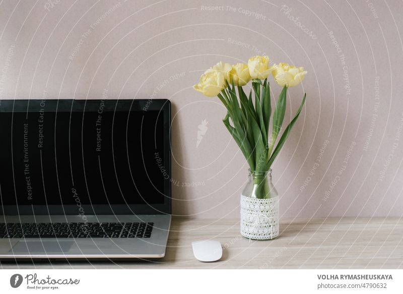 Frühling Heimbüro Stillleben Zusammensetzung. Blank Laptop-Bildschirm. Gelbe Tulpen in einer Vase auf dem Tisch. Büro Arbeitsplatz. Skandinavisches Interieur.