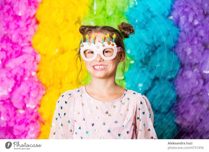 Nettes Mädchen feiert Geburtstag, trägt Party Papier Gläser, lachen und Spaß haben. Heller regenbogenfarbener Hintergrund. Glückliches Ereignis. Kabine hell