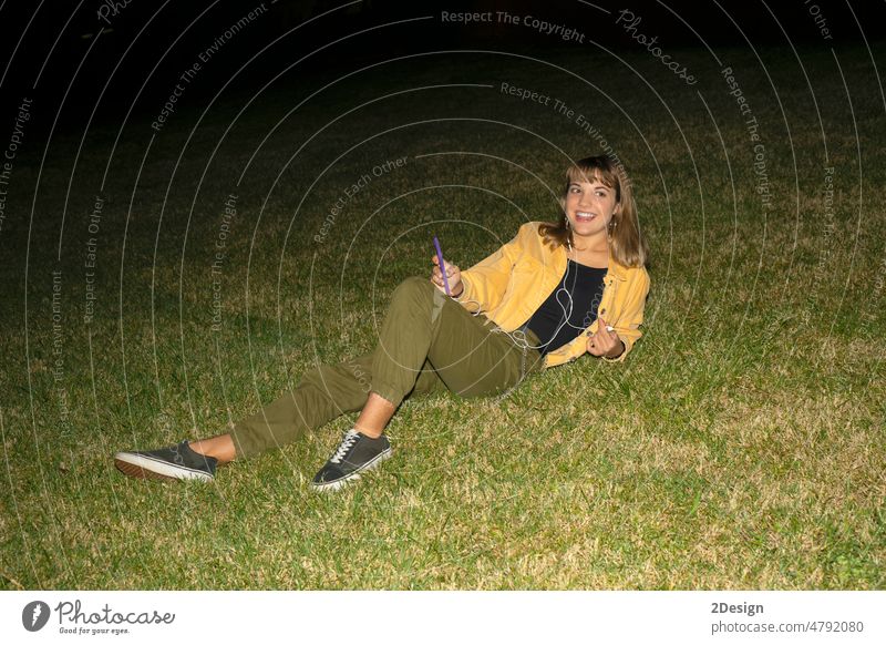 Frau sitzt nachts im Gras in einem Park und benutzt ein Mobiltelefon jung Nacht Sitzen 1 schön attraktiv hübsch Glück Mädchen im Freien Person Lifestyle Porträt