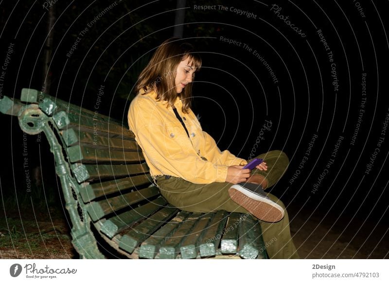 Frau, die mit ihrem Mobiltelefon auf der Bank vor dem Gebäude sitzt Person Telefon im Freien jung Nacht Mobile Sitzen Lifestyle Mädchen Smartphone Glück