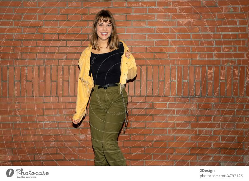 Junge Frau steht in der Nähe einer alten Backsteinmauer in der Stadt bei Nacht jung Stehen attraktiv Lächeln Glück Wand Baustein Freizeitkleidung Person schön