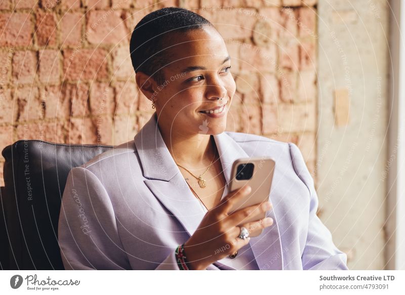 Porträt einer multirassischen LGBTQ-Frau im mittleren Erwachsenenalter, die ein Smartphone benutzt und vor einer freiliegenden Backsteinmauer lächelt