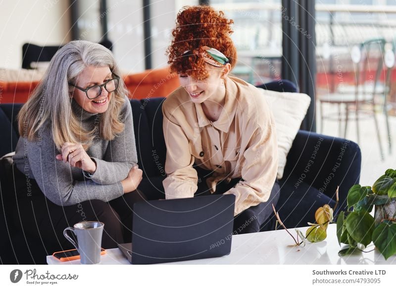 Porträt zweier weißer Geschäftsfrauen, die einen Laptop benutzen und lächeln, ältere Frau mit Brille und junge Frau mit roten Haaren Senior Erwachsener Teamwork