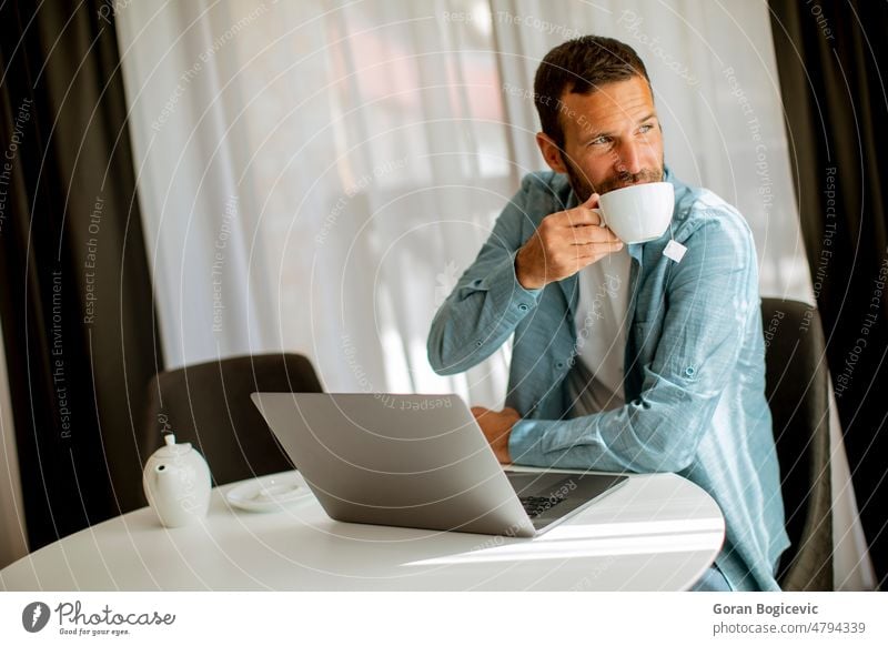 Junger Mann benutzt Laptop und trinkt Tee im Wohnzimmer Lifestyle Tasse Büro Computer modern Business Technik & Technologie trinken Unternehmer Job Internet