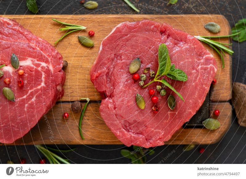 Rohe Rinderfiletsteaks mit Kräutern und Gewürzen auf Holzbrett auf dunklem Hintergrund Nahaufnahme Fleisch Filet Lebensmittel roh Steak rot Rindfleisch frisch