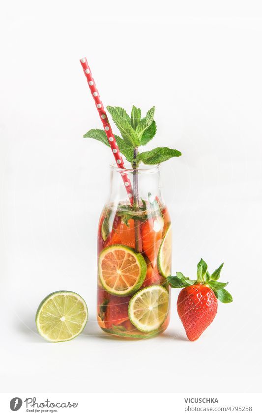 Leckeres Wasser in einer Flasche mit Trinkhalm und Zutaten: Limette, Erdbeere und Minzblätter auf weißem Hintergrund geschmackvoll aufgegossenes Wasser Kalk