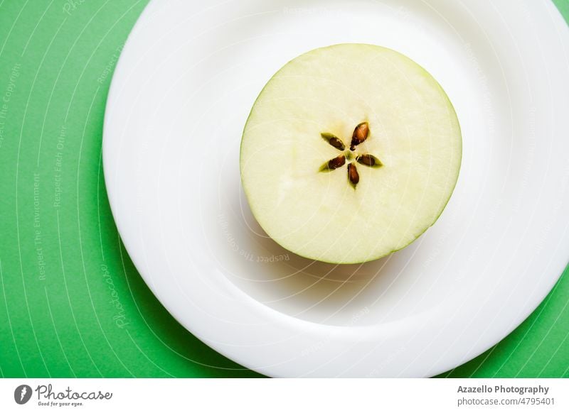 Weißer Teller mit einer Apfelhälfte auf grünem Hintergrund. blau Keramik abschließen kreativ lecker Design Detailaufnahme Diät Spielfigur Essen Fitness