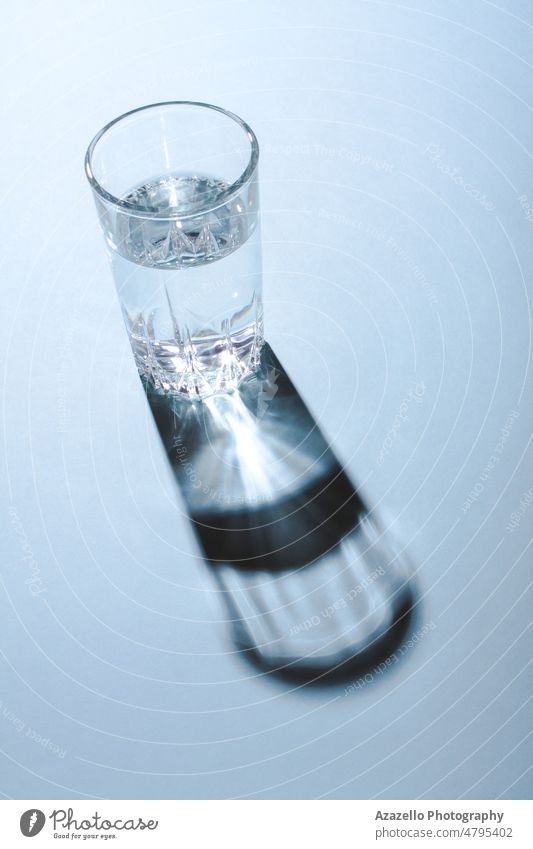 Glas mit sauberem Wasser unter dem hellen Licht, das einen harten Schatten auf blauem Hintergrund wirft. aqua Getränk Körper Sauberkeit sauberes Wasser