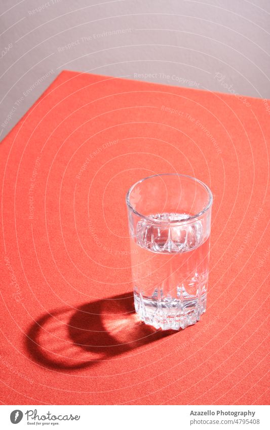 Glas Wasser mit hartem Schatten auf einem Tisch mit rotem Tuch. Kunst Stillleben Tischwäsche abstrakt Material aqua Getränk Körper Sauberkeit sauberes Wasser
