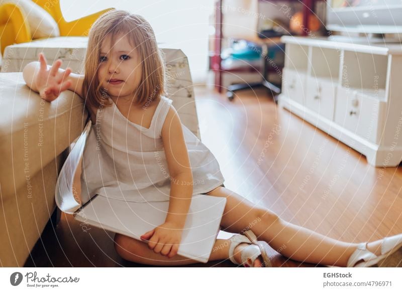 Trauriges kleines Mädchen mit einem Malbuch auf dem Boden im Wohnzimmer sitzend traurig wenig Sitzen Stock Zeichnung Buch Kind Person Kindheit Emotion allein