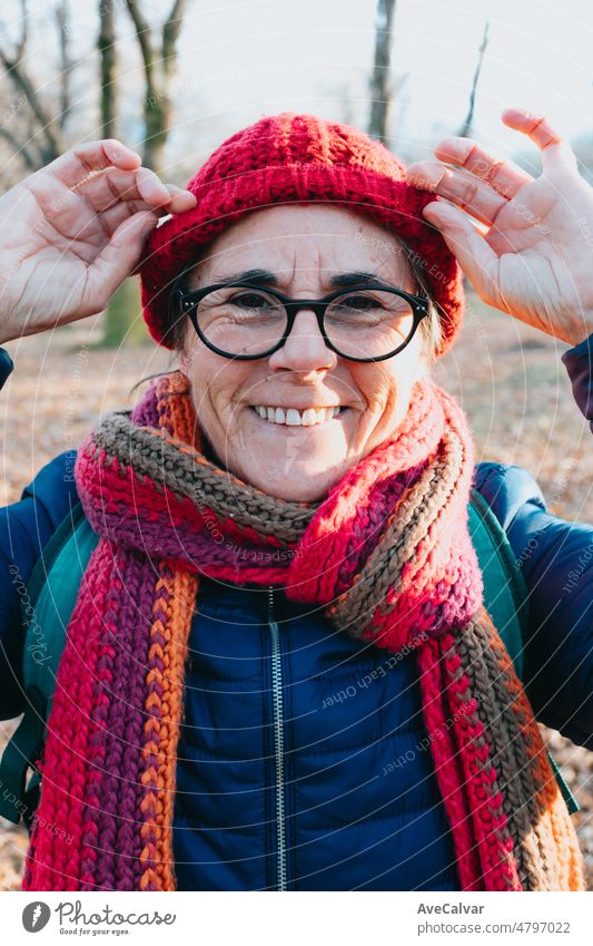 Frontalporträt einer alten Frau, die mit einer Brille in die Kamera lächelt und eine Mütze für die Kälte und den Winter aufsetzt. Aging gut und gesund Konzept, Familie Großmutter Bild. Aktive dritte Alter Konzept