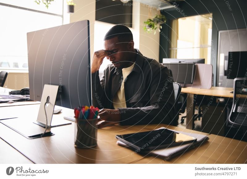 Gestresster schwarzer Geschäftsmann sitzt mit psychischer Erkrankung am Schreibtisch psychische Gesundheit gestresst mental Krankheit Burnout Büro deprimiert