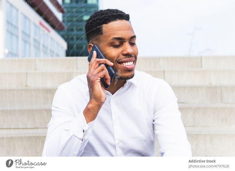Fröhlicher schwarzer Geschäftsmann, der auf der Straße mit seinem Smartphone spricht Unternehmer urban Großstadt Talkrunde Business Telefonanruf Gespräch reden