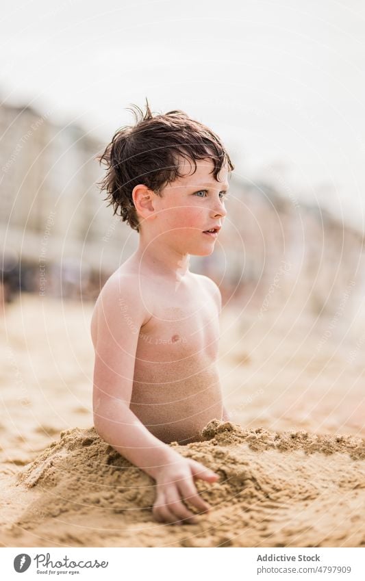 Junge vergräbt sich im Sand und schaut weg Kind spielen vergraben Strand spielerisch sorgenfrei Spiel Küste Sommer Kindheit ruhen Ufer Zeitvertreib Erholung
