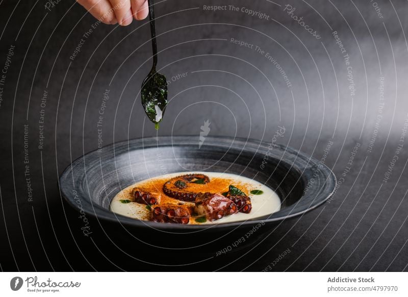 Anonymer Koch mit gebratenem Tintenfisch in Schüssel mit Soße und Paprika Octopus Tentakel Meeresfrüchte dienen Küche kulinarisch Saucen Speise Mahlzeit