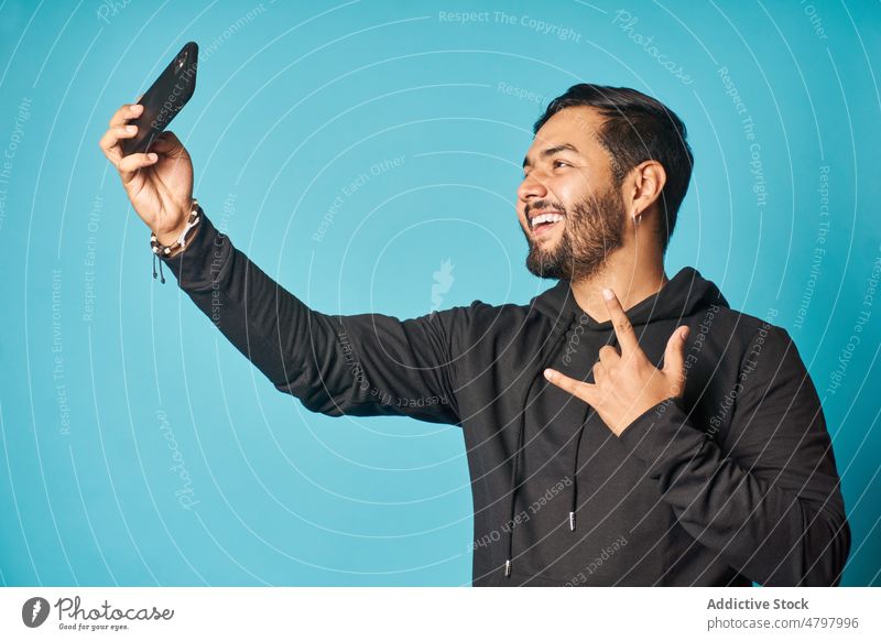 Fröhlicher Mann, der ein Selfie macht, während er das Zeichen der Hörner macht Smartphone Telefon Selbstportrait Rock and Roll soziale Netzwerke Stil Fotografie