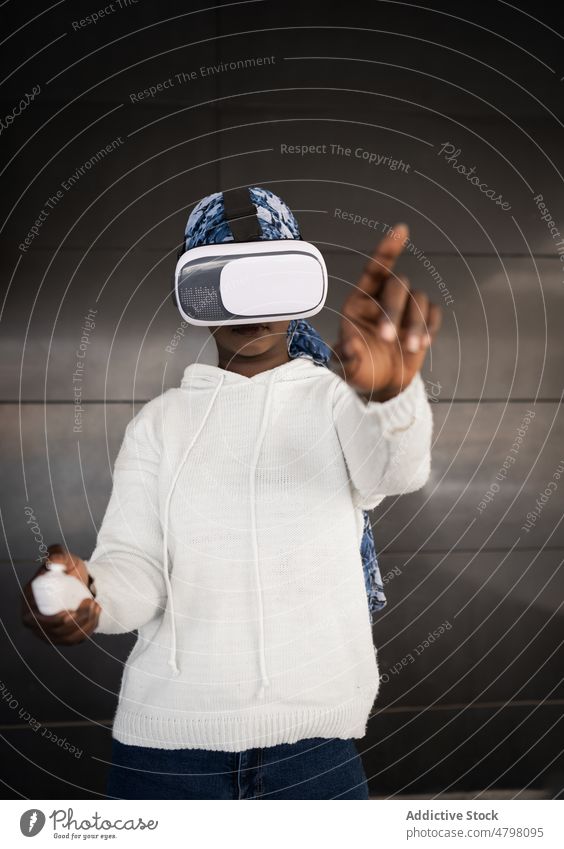 Junge schwarze Frau erkundet den Cyberspace mit einer VR-Brille Virtuelle Realität Regler Erfahrung spielen schieben Kopftuch Headset benutzend Konzentration