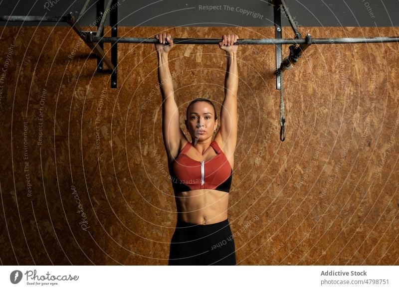 Konzentrierte Sportlerin, die sich beim Training im Fitnessstudio an einer Stange festhält Frau hängen Bar Athlet Konzentration stark Übung Energie Ausdauer