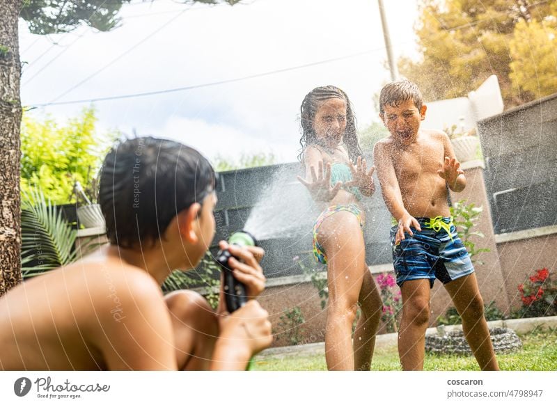 Drei lustige Kinder spielen mit einem Schlauch im Garten aktiv Aktivität Junge Kindheit Tropfen genießen Familie Springbrunnen Freunde Freundschaft Spaß Spiel