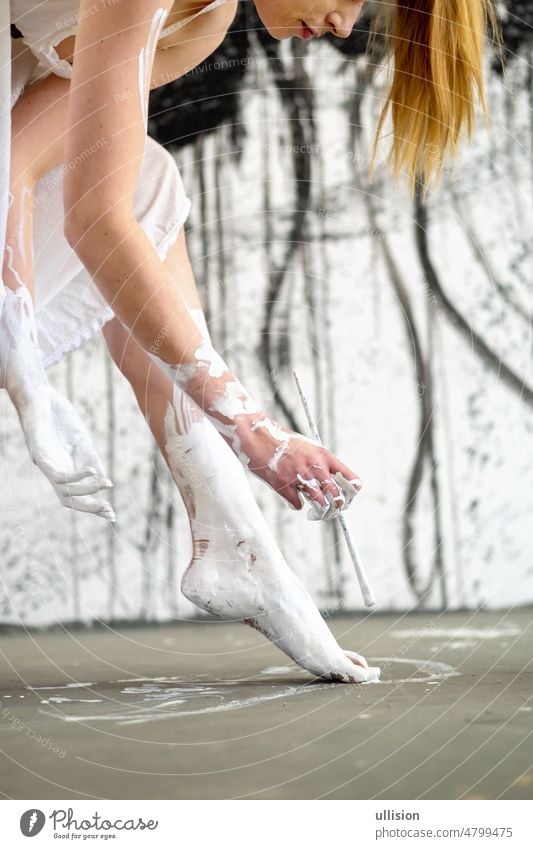 Porträt im Profil einer jungen Frau in weißem Ballettkleid, die einen Pinsel hält und ihre Füße mit Farbe bemalt, vor einem schwarz-weißen künstlerischen Hintergrund.