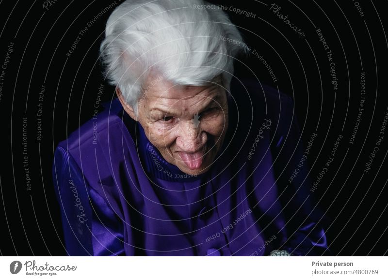 Ältere Frau, Großmutter streckt ihre Zunge heraus lacht Nahaufnahme des Gesichts, Frau zeigt Zunge, Porträt mit offenem Mund und herausgestreckter Zunge.