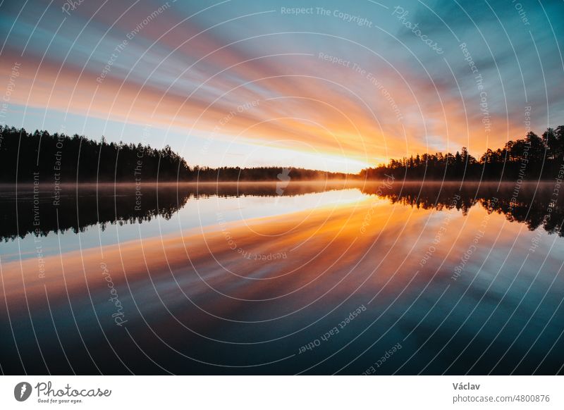 Atemberaubender Sonnenaufgang am Jatkonjärvi-See, der von der Sonne rot, orange, lila, rosa und blau gefärbt wird. Der Nebel, der sich auf der Oberfläche des Sees festsetzt, verleiht dem Schauspiel noch mehr Dramatik. Hossa-Nationalpark, Finnland