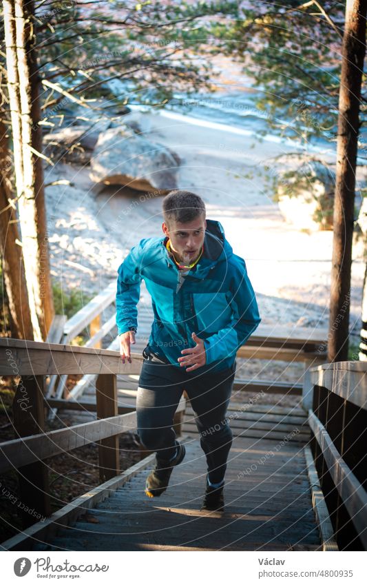 Ein Sportler im Training läuft die Treppe hinauf, um seine Fitness zu verbessern. Ein 20-jähriger Sportler in einer blauen Jacke beim Sommertraining. Sotkamo, Finnland. Aktiver Lebensstil